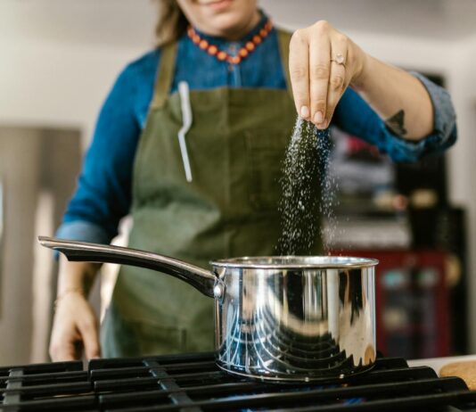 Miért Fontos Figyelni a Sóbevitelre 60 Év Felett Nő túl sok sót szór a főzőedénybe a konyhában, figyelmeztetés a túlzott sófogyasztás veszélyeire