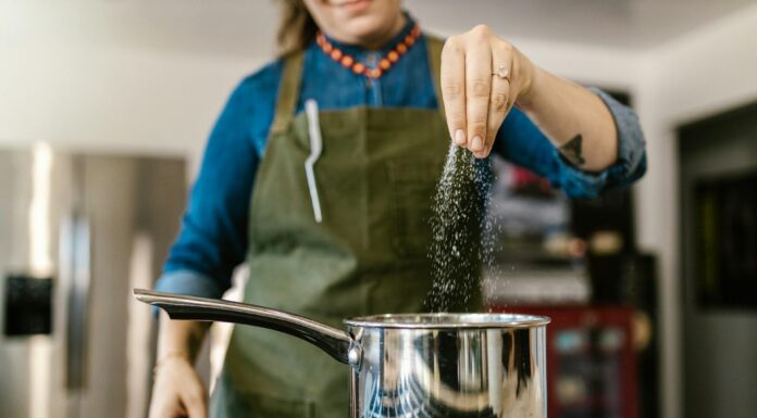 Miért Fontos Figyelni a Sóbevitelre 60 Év Felett Nő túl sok sót szór a főzőedénybe a konyhában, figyelmeztetés a túlzott sófogyasztás veszélyeire
